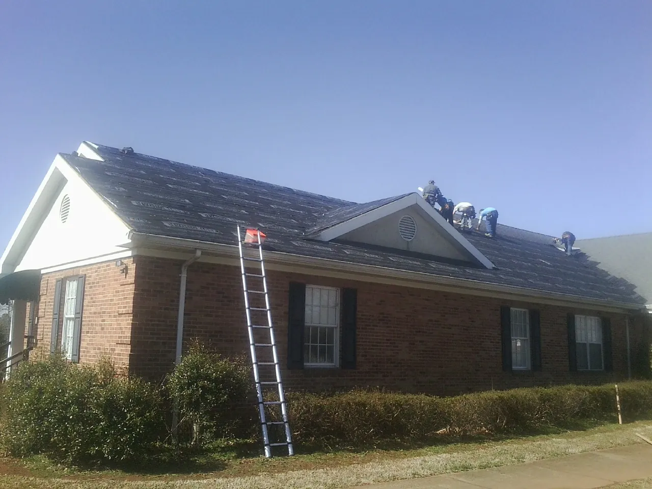 Crew tearing shingles off a brick ranch roof with a ladder set — Emergency Roof Repair work by our crew in Kahoka