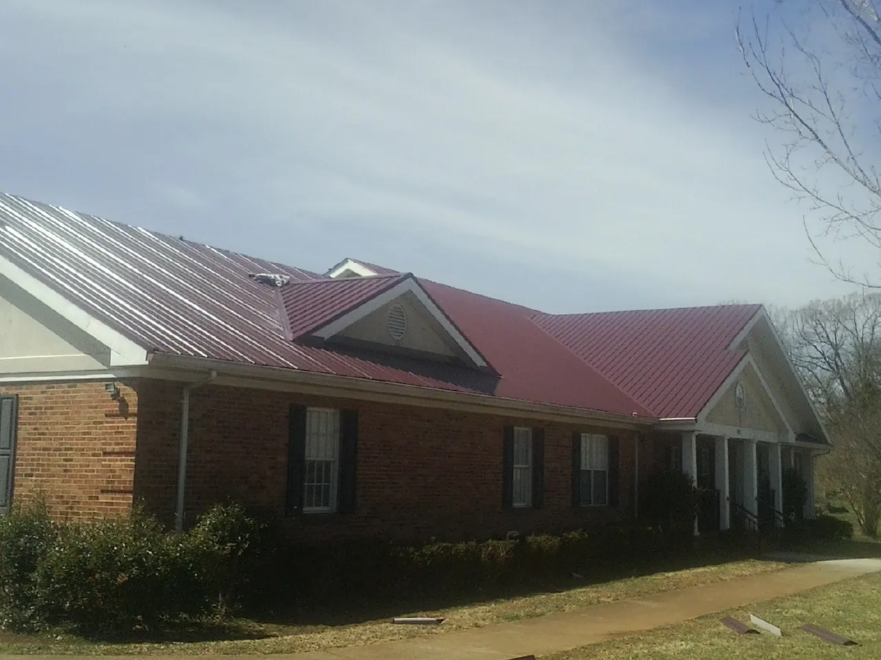 Red metal roof with gabled entries on a long brick building, from a Hail Damage Roof Repair job in Kahoka