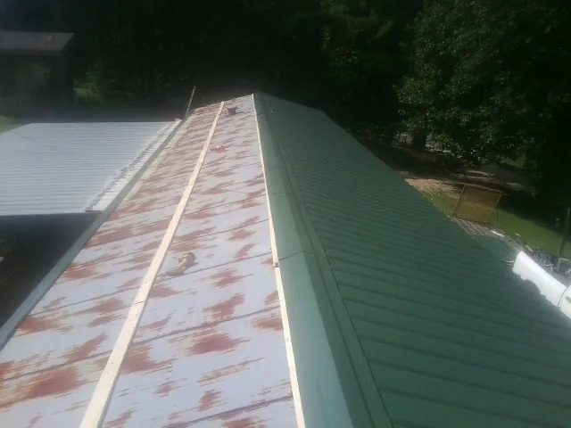 Old rusted panels beside newly installed green metal roofing — Wind Damage Roof Repair by Roofing Brothers in Kahoka