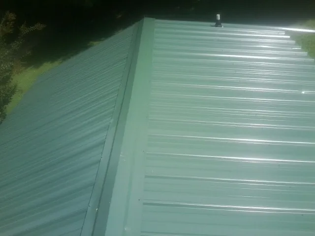 New green metal panels meeting at the ridge of a roof — Flat Roof Repair work by our crew in Kahoka