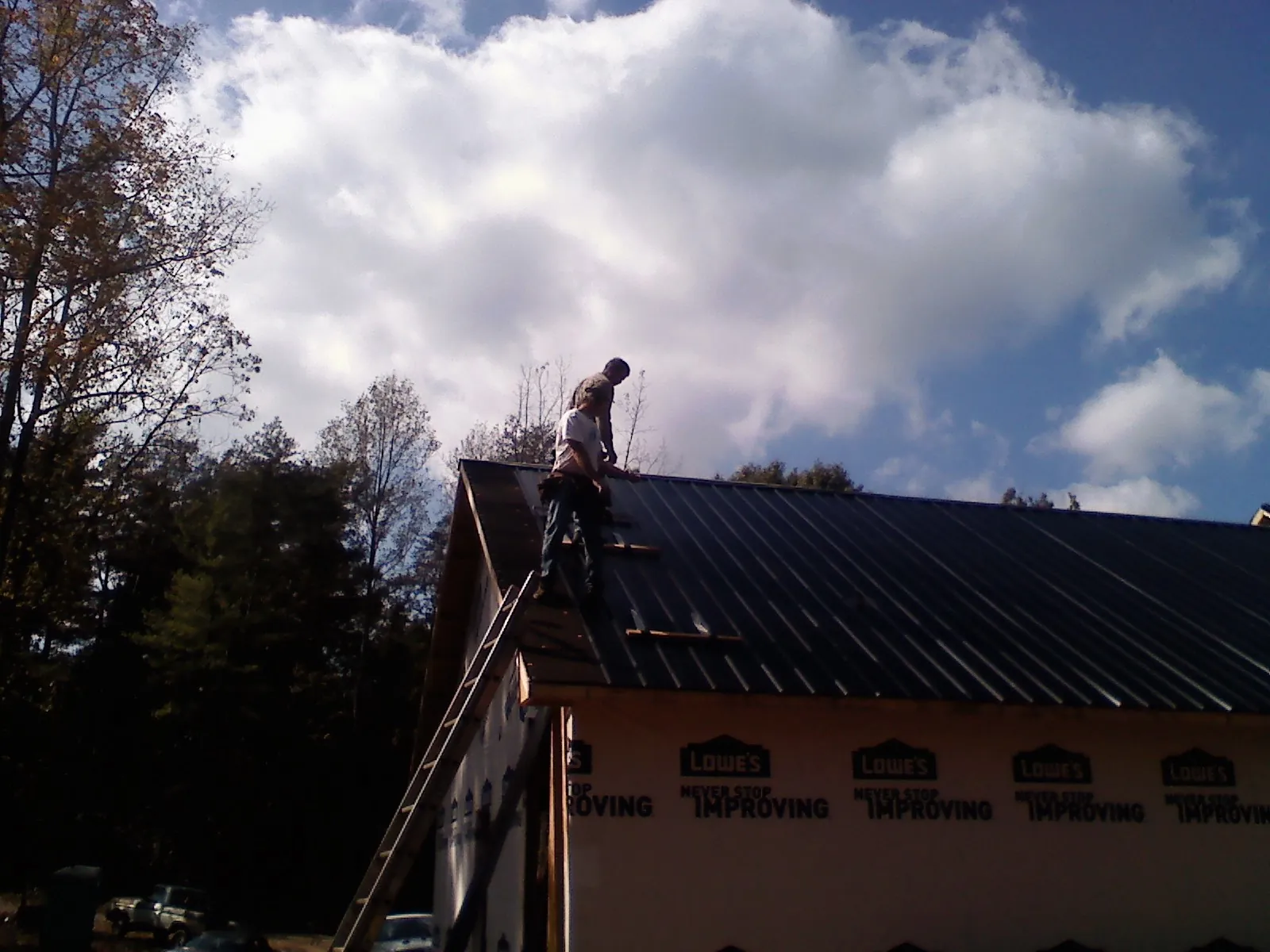 Roofer fastening dark metal panels high against a cloudy sky, from a Roof Inspection job in Kahoka