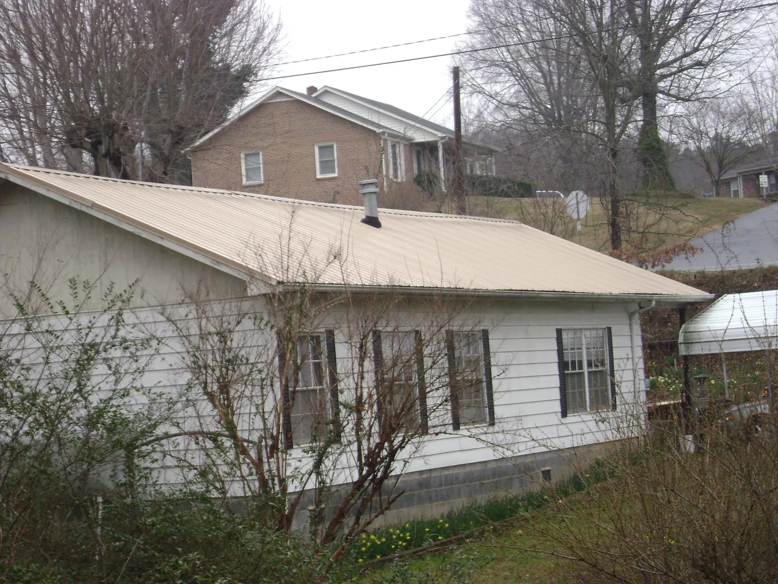 Tan metal roof on a white sided house set into a hillside — Commercial Roofing by Roofing Brothers in Kahoka